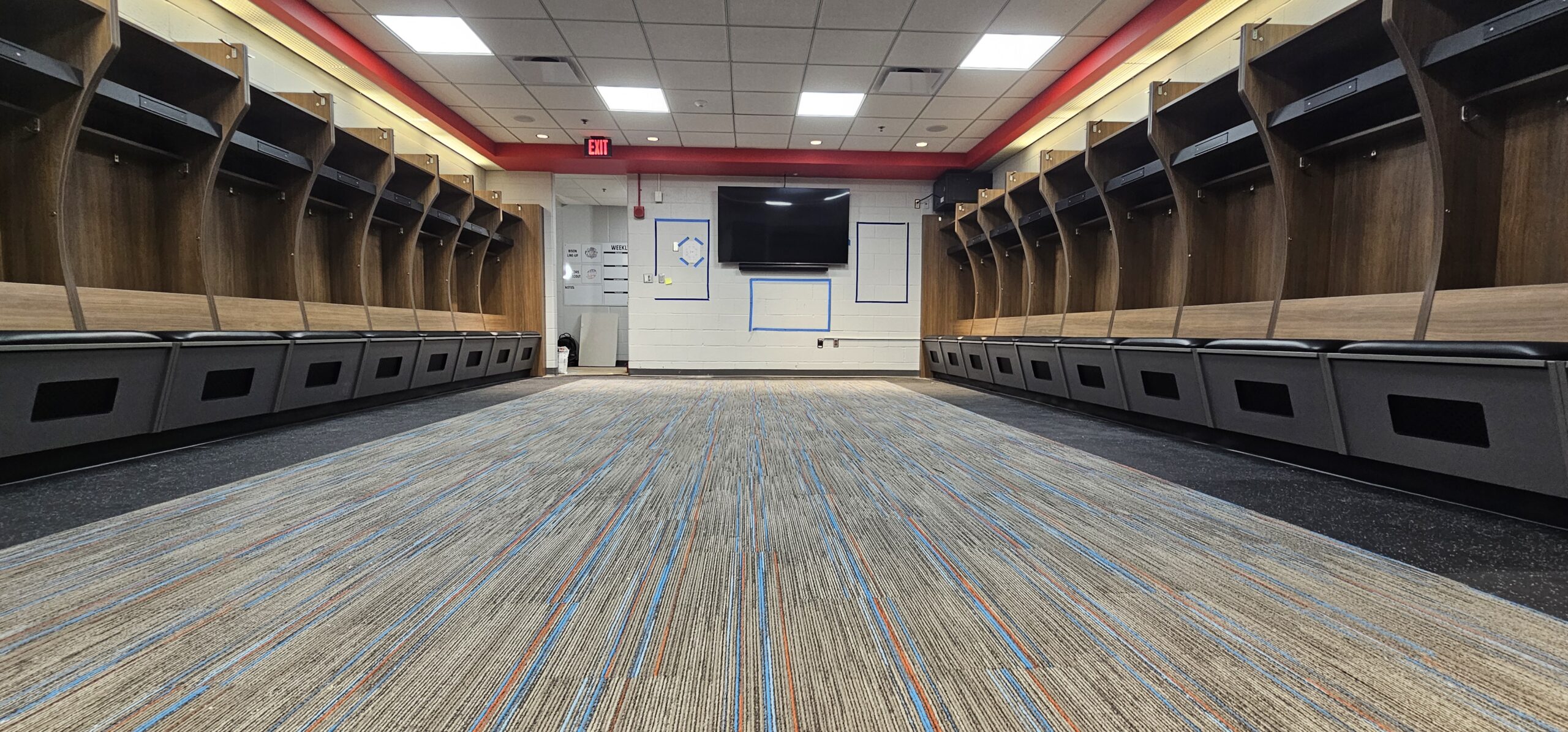 Photo of custom hockey locker room seating. The wood is walnut and gray, and the seats are padded with black cushions.